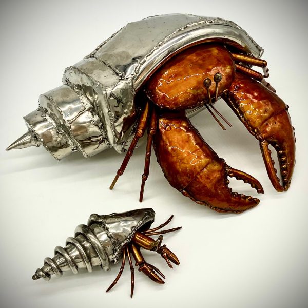 A hermit crab, glinting in polished stainless steel, carries its home on its back.