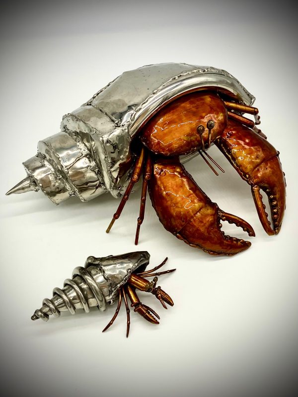 A hermit crab, glinting in polished stainless steel, carries its home on its back.