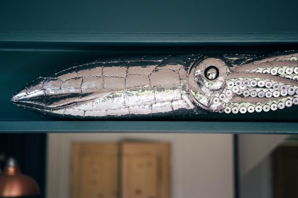 Gleaming stainless steel captures the form of a squid in this wall sculpture.