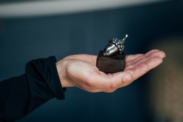 A miniature acorn, crafted from stainless steel, finds its home on a wooden platform.