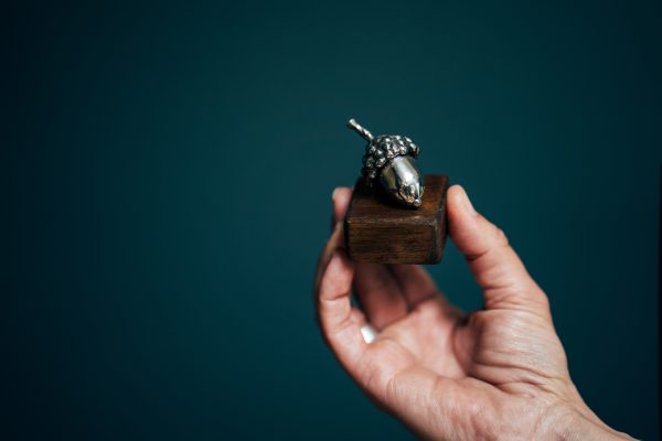 From seed to sculpture: a tiny acorn crafted from gleaming metal rests on wood.