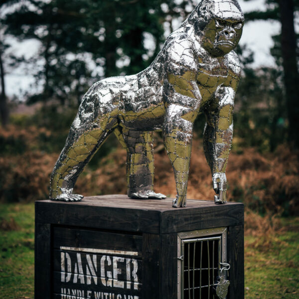 Stainless steel gorilla garden ornament on a wooden base.