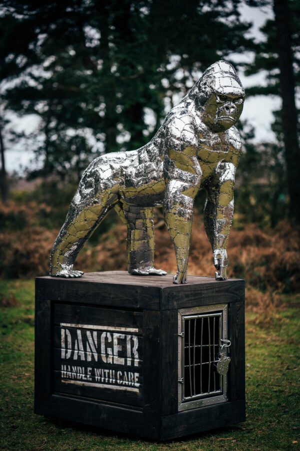 Stainless steel gorilla garden ornament on a wooden base.